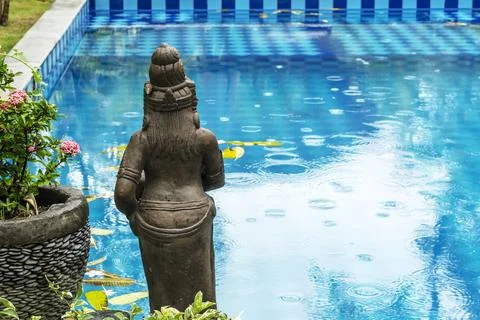 A statue by the pool in the rain within a tropical garden. The water is cover Foto stock