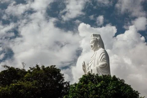 Statue of white Buddha surrounded by trees against the sky, asia Stock Photos