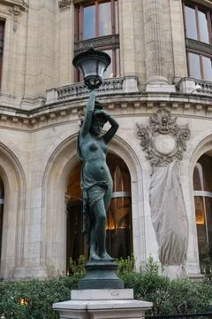 Statue of a woman holding a lamp in front of an elegant historical building.. Stock Photos