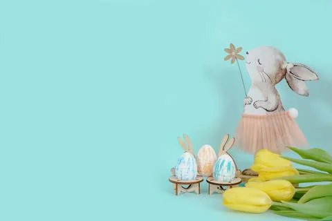 Statuette of an Easter bunny with colored eggs on a blue background with fresh Stock Photos