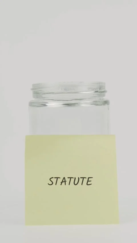 Statute text or word on yellow sticky note attached to glass jar with hand Stock Footage 311789434
