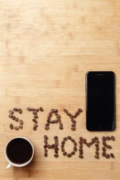 Stay Home slogan made of coffee beans, a smartphone and a cup of brewed coffee Stock Photos