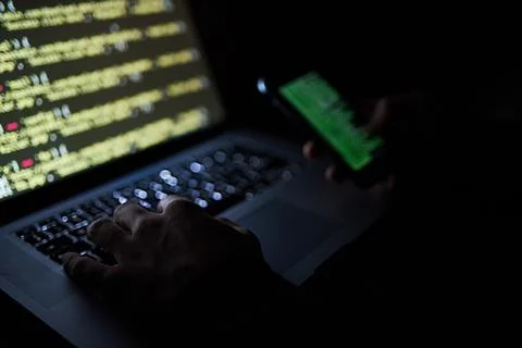 Staying focussed on the code. an unidentifiable hacker using a laptop late at Stock Photos