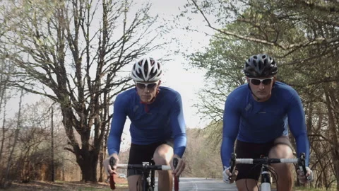 Steadicam  close up shot faces of two healthy men peddling fast with cycling roa Stock Footage 199630963