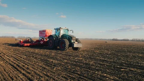 Steadicam pan shot: A tractor with a large seeder is driving across the field in Stock Footage 74462425