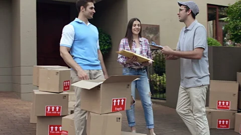 Steadicam shot of delivery man or courier, delivery parcel to happy couple while Video stock 199631901