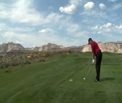 Steadicam shot as man tees on golf course with red rock cliffs and distance Stock Footage
