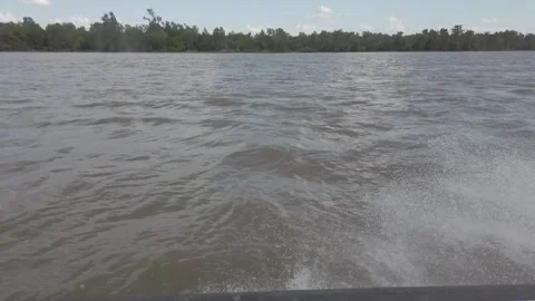 Steadicam shot from right side boat on river with splashes and forest on coast Stock Footage 164893473