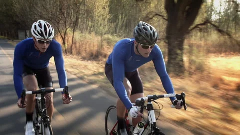 Steadicam shot of two healthy men peddling fast with cycling road bicycle at sun Stock Footage 199630964