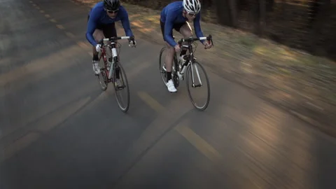 Steadicam shot of two healthy men peddling/ free wheeling  down hill with cyclin Stockbeeldmateriaal 199630974