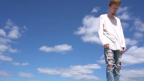 Steadicam shot of a young red haired stilish man against blue sky background. Stock Footage 76442870