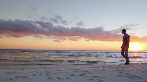Steadicam slow motion shot: Young lonely man walking along the seashore at Stock Footage 67622655