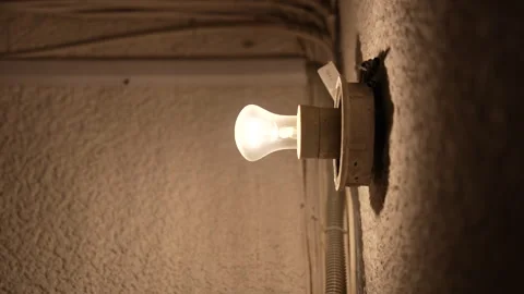 Steady glowing light bulb on textured wall in vintage apartment corridor Vidéo 325802131