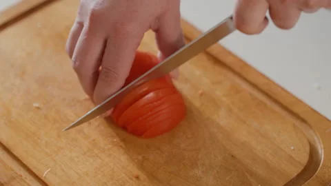 Steady hand slicing ripe red tomato into thin even pieces on wooden cutting Stock Footage 343676796