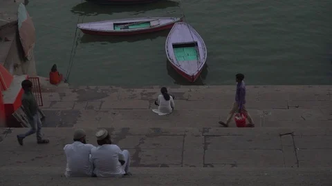 Steady handheld shot of two men sitting on the stairs of a ghat Stock Footage 114659685