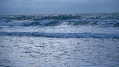 Steady shot of rhythmic ocean waves rolling towards the sandy beach at dusk Vídeos de archivo 342025227