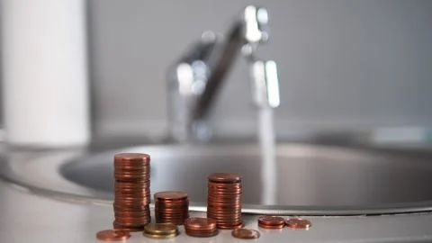 A steady stream from a faucet flows behind neatly stacked columns of coins The Stock Footage 286134456