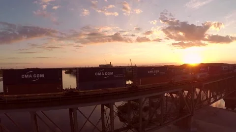 Steadycam shot of a train on a bridge over a river while the sun goes down Stock Footage 43887858