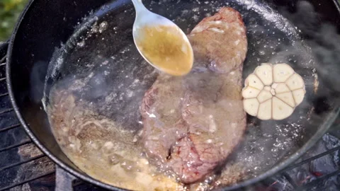 A steak is being cooked on a grill. The chef spoons melted butter onto the steak Stock Footage 315278991