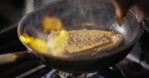 Steak being turned on frying pan with open flame of grill Stock Footage 274652991