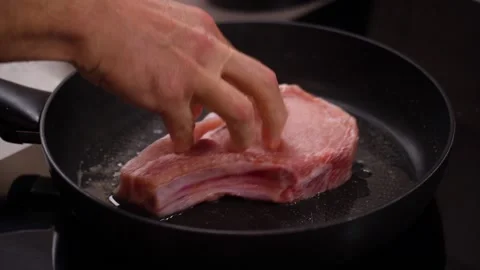 Steak, meat on the bone hand puts on a frying pan to fry Vidéo 232780219