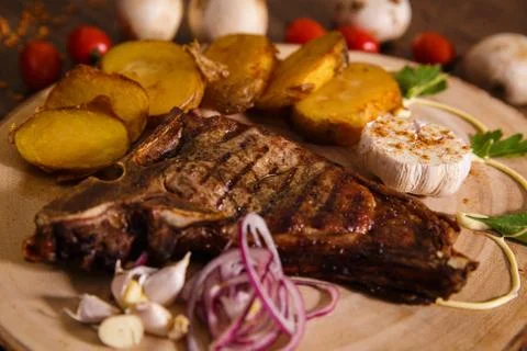 Steak t-bone on wooden backing and baked potatoes Stock Photos