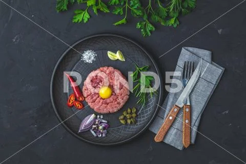 Steak tartare with yolk and ingredients on black ceramic plate Stock Photos