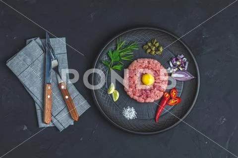 Steak tartare with yolk and ingredients on black ceramic plate Stock Photos