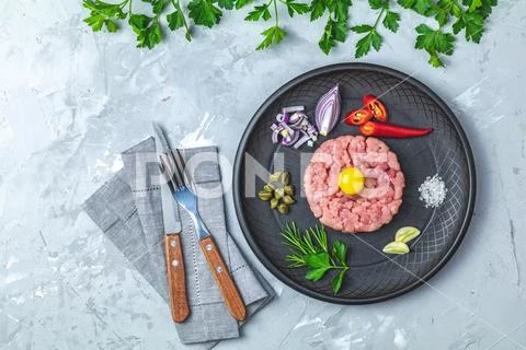 Steak tartare with yolk and ingredients on black ceramic plate Stock Photos