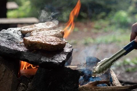 Steaks are fried on a stone in a fire in nature Stock Photos