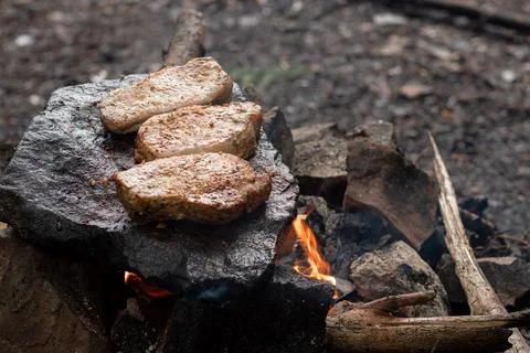 Steaks are fried on a stone in a fire in nature Stock Photos