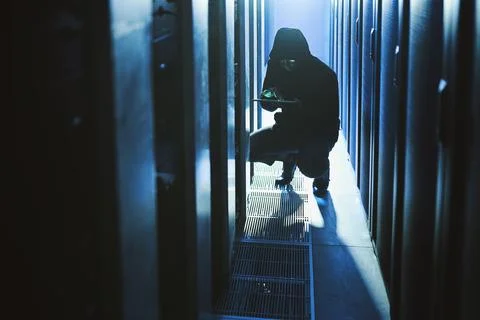 Stealing all of your data. a hacker using a digital tablet in a server room. Stock Photos