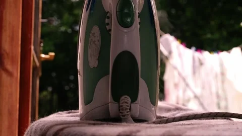 Steam iron with laundry hanging on line in background Stock Footage 277280757