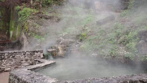 Steam rises from a natural hot spring waterfall in a lush forest setting. Stock Footage 345616438