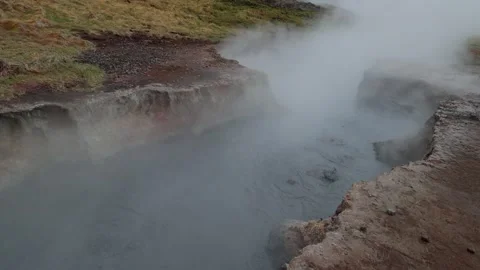 Steam rising from a bubbling geothermal mud pot in a volcanic landscape under Stock Footage 339303783
