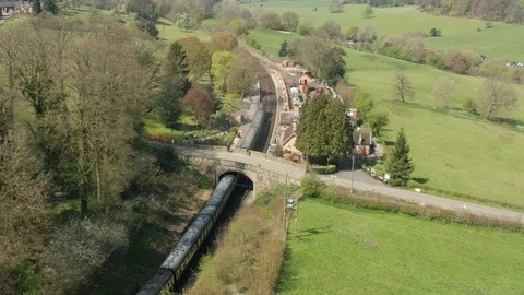 Steam train arriving at UK countryside railway station Stock Footage