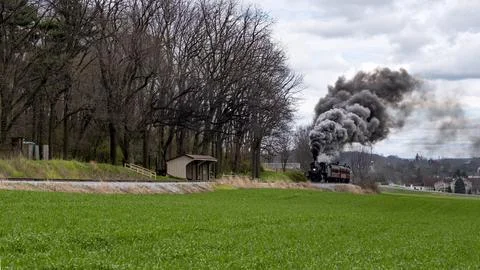 Steam Train Billows Smoke While Passing Through Lush Green Fields Near a Ru.. Stock Photos