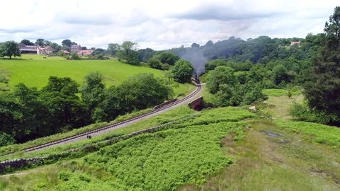 Steam train drone shot appearing around a corner in Yorkshire Stock Footage 240623458