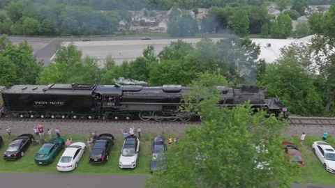 A steam train known as Big Boy travels along the tracks beside a row of parked Stock Footage 341114593