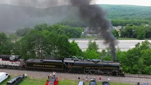 A steam train moves along the tracks near a river while people gather in the Stock Footage 340406208