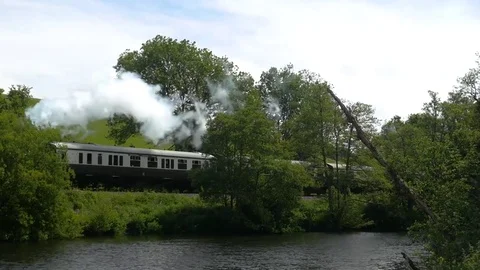 Steam train passing besides a river, panning shot Stock Footage 76530273
