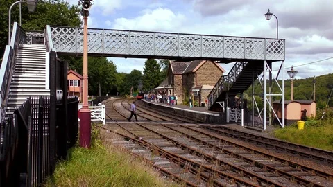 Steam train pulling into country station under footbridge Stock Footage 80319718