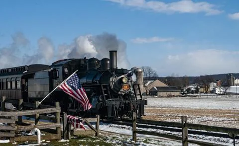Steam train is pulling train car with American flag. The train is traveling Stock Photos