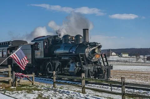 Steam train is pulling train car with American flag. The train is traveling Stock Photos