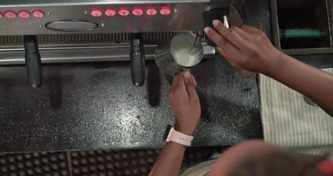Steam wand is texturing milk in stainless pitcher while control knob is being Stock-Footage 343240392
