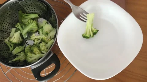 Steamed broccoli, picking from a pot on a white plate. Stock Footage 132780081
