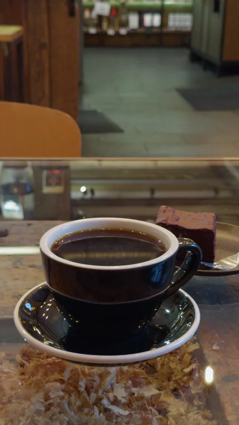 Steaming black coffee cup on saucer beside chocolate dessert in cozy cafe Stock Footage 346558797