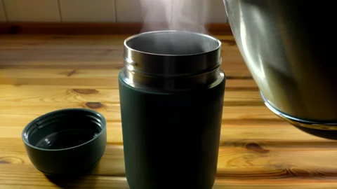 Steaming boiling water pouring from a kettle into an insulated steel cup. Video stock 170257495