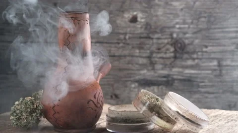 Steaming bong with cannabis on the table on which there is a grinder and a large Video stock 134940434