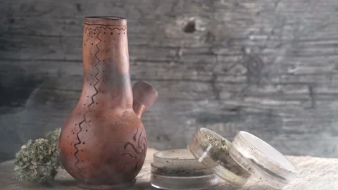 Steaming bong with cannabis on the table on which there is a grinder and a large Stock Footage 134940504